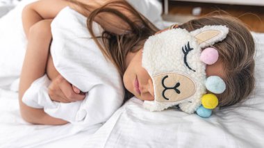 Küçük bir kız yastıkta uyuyor. Sabahları komik bir uyku maskesi takıyor..