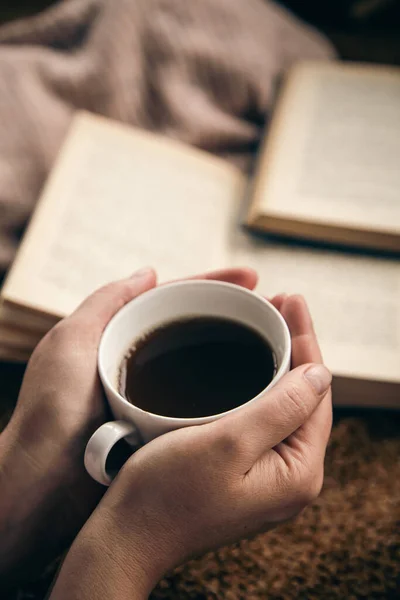 Close-up, a cup of tea in female hands on a blurred book background, the concept of reading and leisure.