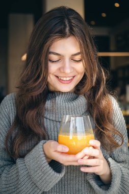 Bir bardak taze sıkılmış portakal suyuyla gülümseyen çekici genç kadın..