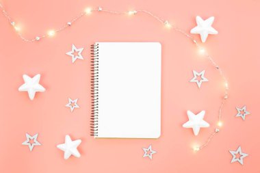 Yıldızlı boş bir defter, defterin yanına çelenk serpilmiş. Bir dilek listesi, hediyeler veya yıl için hedefler.