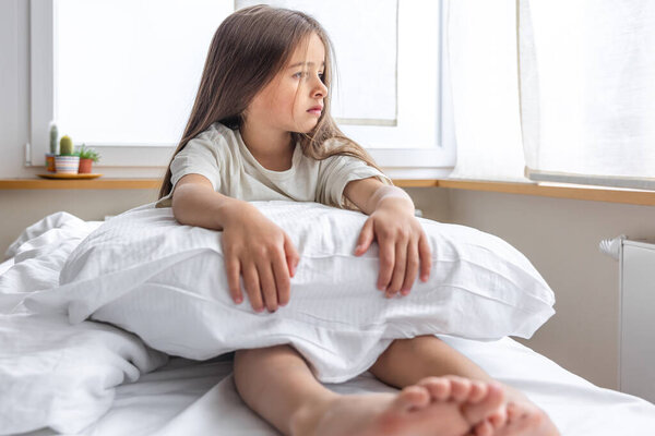 Adorable little girl with pillow in bed early in the morning.