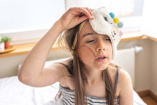Portrait of an adorable little girl with a sleep mask, waking up in her bed on a sunny morning.