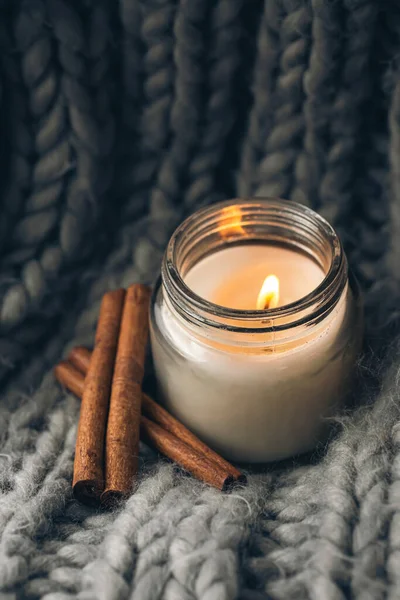 Close-up, aromatic candle and cinnamon sticks on the background of a gray knitted element.