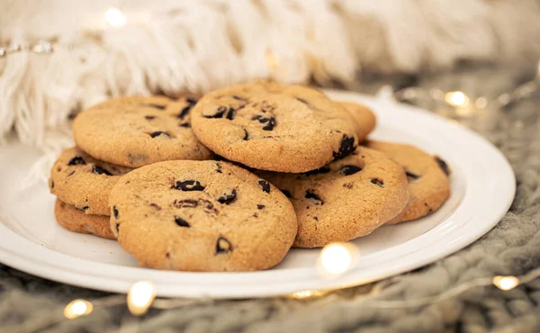 Close-up of chocolate chip cookies on a plate on a blurred background with a garland.