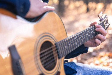 Yakın plan, bir adam soğuk mevsimde ormanda akustik gitar çalar..