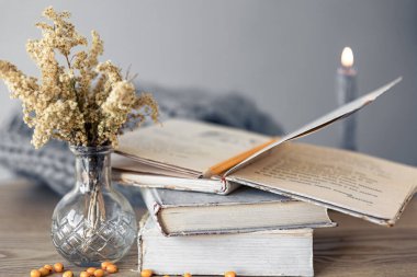 Bir yığın kitap, kurutulmuş çiçekli bir vazo ve odanın içinde bulanık bir arkaplanda bir mum..
