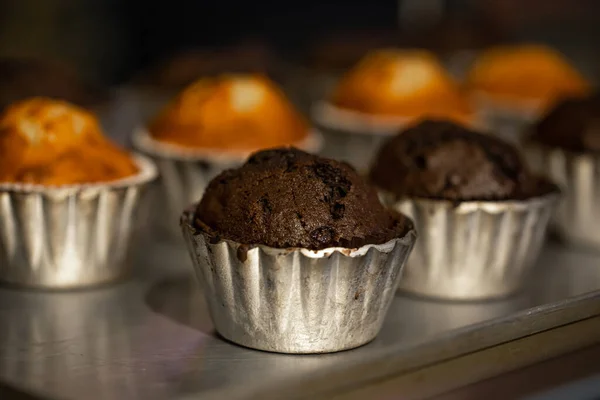 stock image Freshly baked muffins in metal molds close-up in a bakery on a dark blurred background.