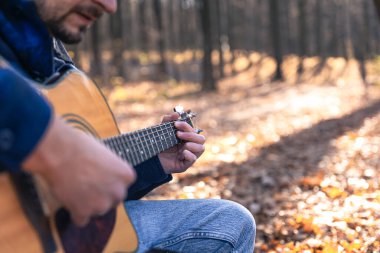 Yakın plan, bir adam soğuk mevsimde ormanda akustik gitar çalar, uzayı taklit eder..