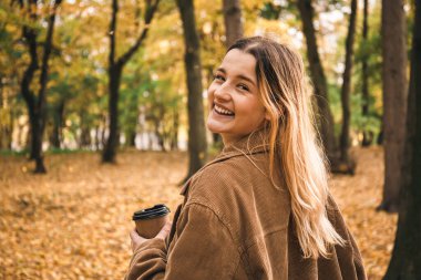 Güz ormanında arka planda bir fincan kahveyle çekici genç bir kadın. Bulanık arka planda..