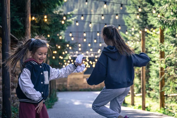 Two little girls dance in a forest in a mountainous area on a blurred background with light bulbs.