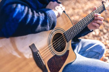 Yakın plan, bir adam soğuk mevsimde ormanda akustik gitar çalar..