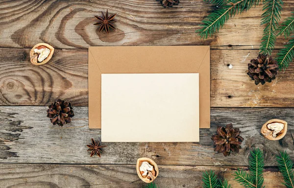 stock image Blank paper, envelope on a wooden background with Christmas tree branches and cones, flat lay.