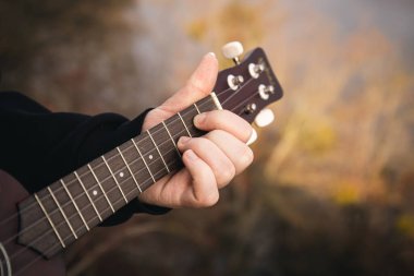 Bir adam doğada gitar çalar, yakın plan parmaklar telleri sıkar, arka plan bulanıklaşır, boşluk kopyalar..