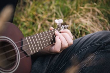 Bir adam doğada gitar çalar, yakın plan parmaklar telleri sıkar, arka plan bulanıklaşır, boşluk kopyalar..
