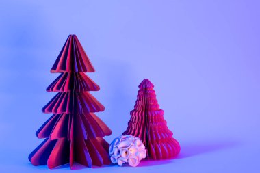 Minimalist yaratıcı Noel ve yeni yıl sanat kompozisyonu. Mavi arka planda, neon ışıklı kağıt köknar ağaçları. Boşluğu kopyala, metin için boşluk.