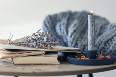Bulanık arkaplanda bir yığın kitap ve bir mum ile rahat ev kompozisyonu.