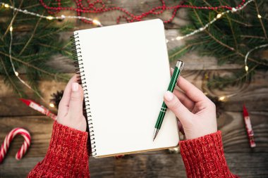 Beyaz not defteriyle birlikte Noel arkaplanı. Güzel kadın elleri, bir kız gelecek için planlar, hedefler yazar..