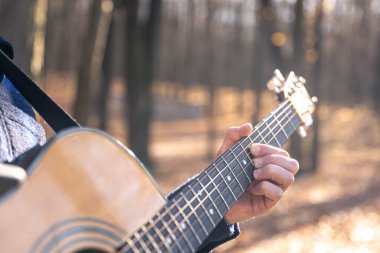 Yakın plan, bir adam soğuk mevsimde ormanda akustik gitar çalar..