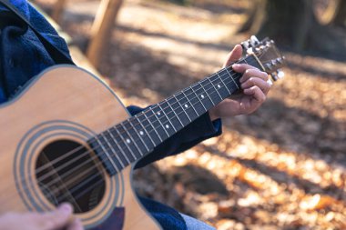 Yakın plan, bir adam soğuk mevsimde ormanda akustik gitar çalar..