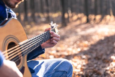Yakın plan, bir adam soğuk mevsimde ormanda akustik gitar çalar, uzayı taklit eder..