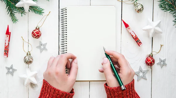 stock image Festive Christmas background with white notepad sheet. Beautiful female hands, a girl writes plans, goals for the future, flat lay.