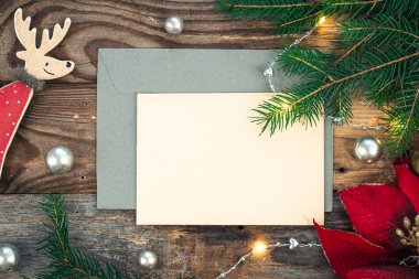 Boş kağıt, zarf, ladin dalları ve ahşap arka planda samimi Noel dekorasyonu ayrıntıları, düz uzanma.