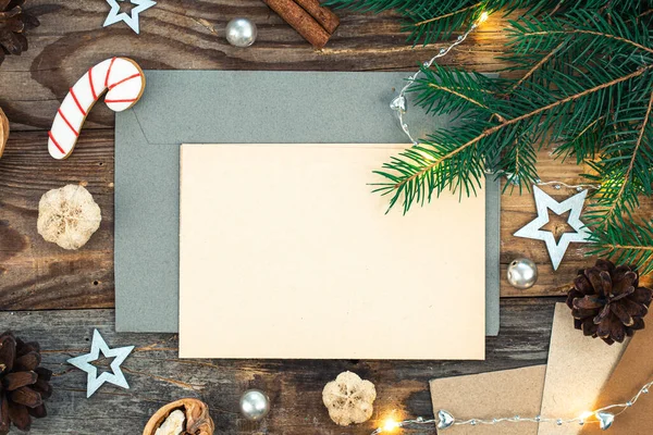 stock image Blank paper, envelope, spruce branches and cozy Christmas decor details on wooden background, flat lay.