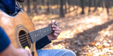 Yakın plan, bir adam soğuk mevsimde ormanda akustik gitar çalar, uzayı taklit eder..