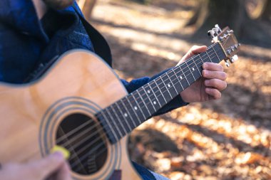 Yakın plan, bir adam soğuk mevsimde ormanda akustik gitar çalar..