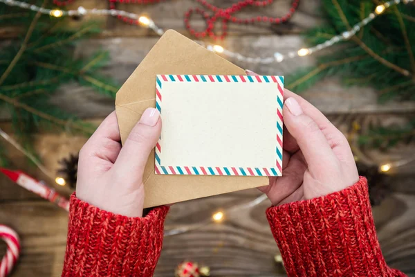 一个女人手里拿着一张空白的圣诞卡和一个信封 在模糊的背景下 是节日装饰的细节 顶视图 — 图库照片