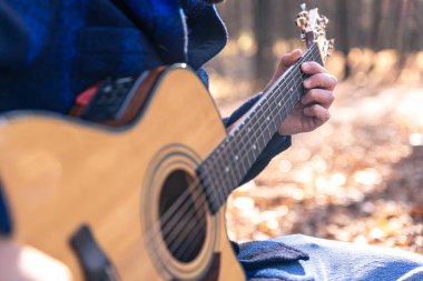 Yakın plan, bir adam soğuk mevsimde ormanda akustik gitar çalar, uzayı taklit eder..