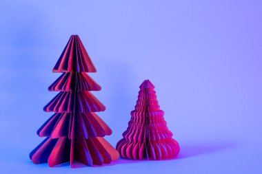 Minimalist yaratıcı Noel ve yeni yıl sanat kompozisyonu. Mavi arka planda, neon ışıklı kağıt köknar ağaçları. Boşluğu kopyala, metin için boşluk.