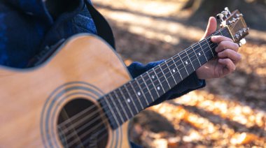 Yakın plan, bir adam soğuk mevsimde ormanda akustik gitar çalar..