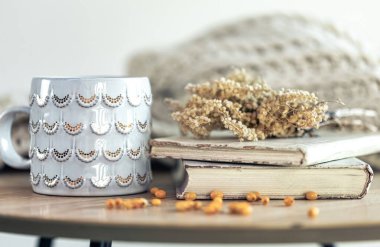 Bir yığın kitap, güzel bir fincan ve odanın içinde bulanık bir arka planda kurumuş çiçekler..