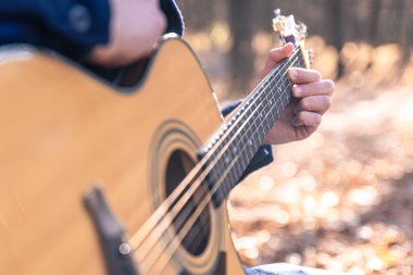 Yakın plan, bir adam soğuk mevsimde ormanda akustik gitar çalar, uzayı taklit eder..