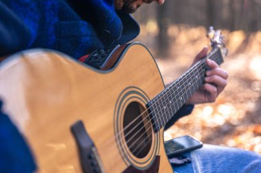 Yakın plan, bir adam soğuk mevsimde ormanda akustik gitar çalar..