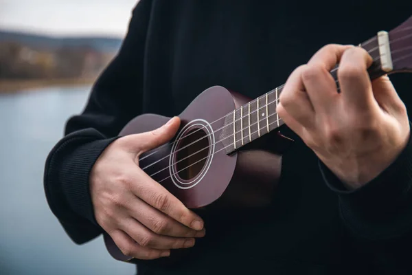 Genç Bir Adam Ukulele Gitarını Doğada Nehrin Bulanık Arka Planında — Stok fotoğraf