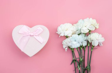 Bir buket çiçek, pembe arka planda kalp şeklinde bir hediye kutusu, kadınlar günü konsepti, doğum günü..