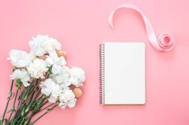 Boş not defteri ve çiçek buketi ve pembe arka planda kalp şeklinde bir hediye kutusu, düz konum, kopyalama alanı.
