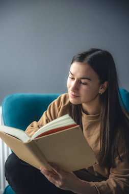 Genç bir kadın sandalyede oturmuş kitap okuyor, boşluğu kopyalıyor..