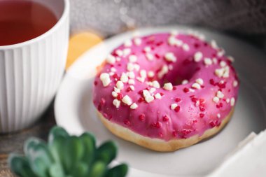 Pembe bir donut, bir fincan çay ve örgü elementi ile rahat bir kompozisyon..