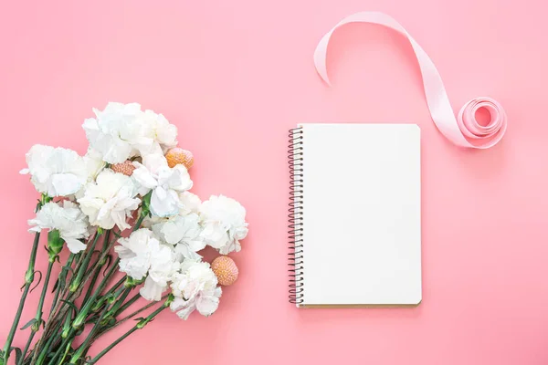 Blank notepad and flower bouquet and heart shaped gift box on a pink background, flat lay, copy space.