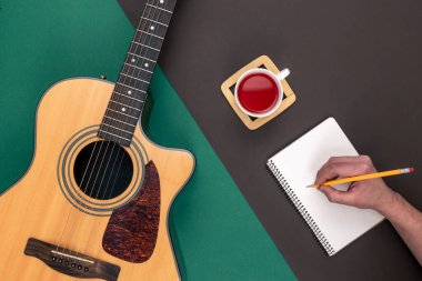 Düz konum, akustik gitar, bir fincan çay ve arka plan üzerine not defteri, müzik yapımı ve yaratıcılık kavramı.