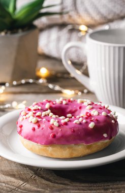 Pembe bir çörek, bir fincan çay ve örülmüş bir elementle rahat ev kompozisyonu..