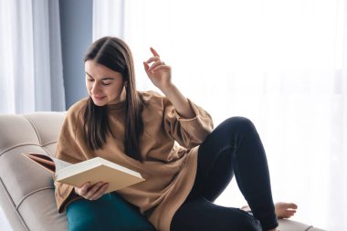 Pencerenin yanındaki koltukta oturan genç bir kadın kitap okuyor, boşluğu kopyalıyor..