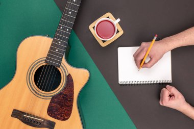Düz konum, akustik gitar, bir fincan çay ve arka plan üzerine not defteri, müzik yapımı ve yaratıcılık kavramı.