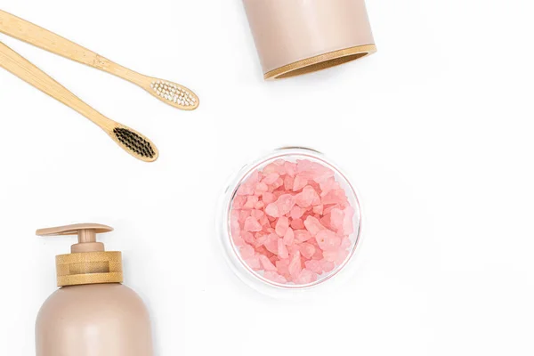 Close-up, pink sea salt, toothbrushes and liquid soap dispenser on white background, top view.