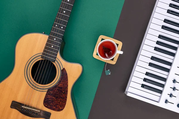 Acoustic guitar, musical keys and a cup of tea on a colored background, top view.
