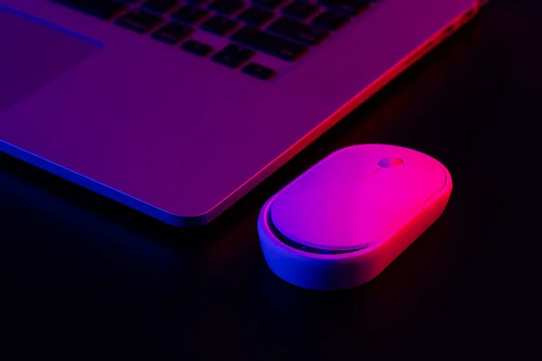 Computer mouse near laptop in neon lighting, close-up, night work concept.