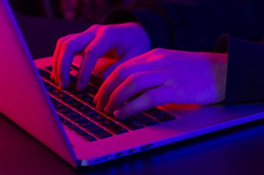 Bir adam dizüstü bilgisayar kullanıyor, yakın plan, erkek eli neon ışıklı, gece çalışma konsepti.